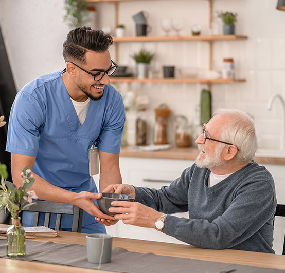 Smiling friendly caretaker serving breakfast to a pensioner